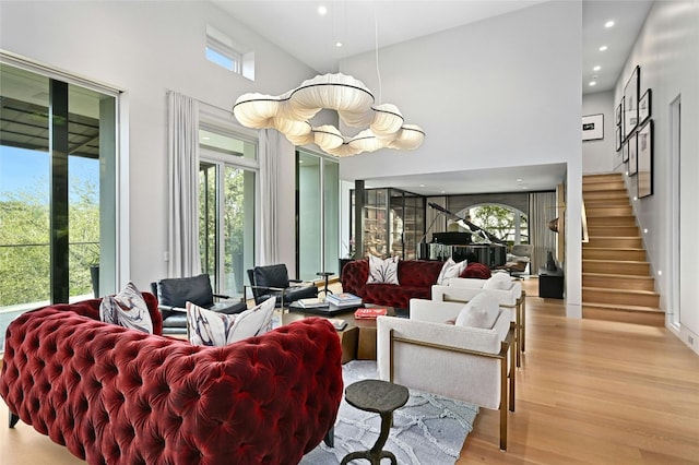 living area featuring plenty of natural light, light wood-style floors, a towering ceiling, and stairs