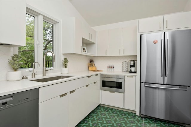 kitchen with a sink, backsplash, appliances with stainless steel finishes, white cabinets, and light countertops