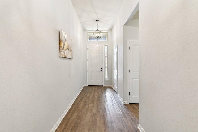 doorway with a healthy amount of sunlight, wood finished floors, baseboards, and a chandelier