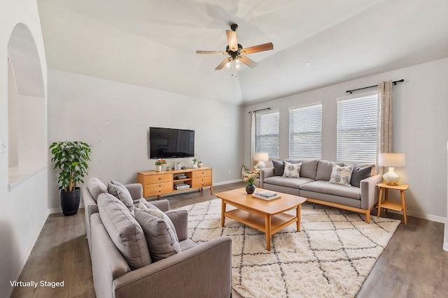 living room featuring wood finished floors, arched walkways, baseboards, ceiling fan, and vaulted ceiling