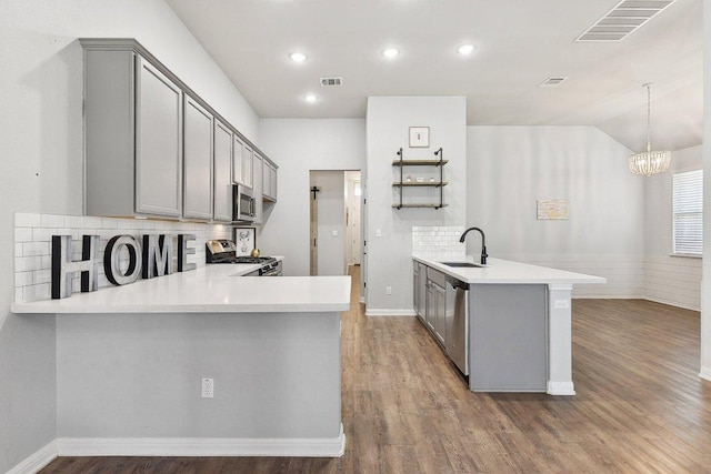 kitchen with visible vents, a peninsula, a sink, gray cabinetry, and appliances with stainless steel finishes