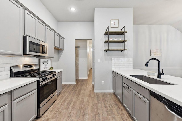 kitchen featuring gray cabinets, a sink, open shelves, appliances with stainless steel finishes, and light countertops