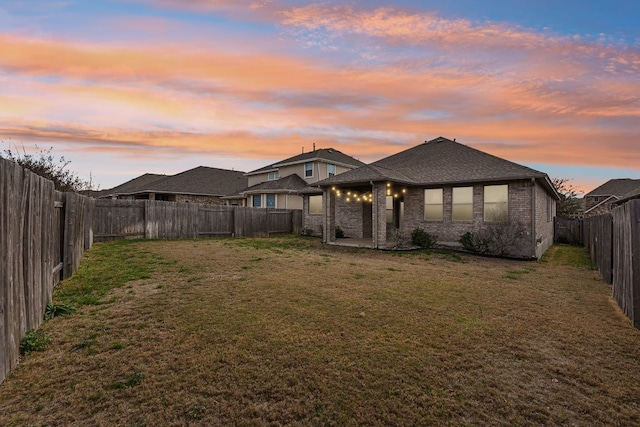 back of property at dusk with a lawn, a fenced backyard, brick siding, and a patio area