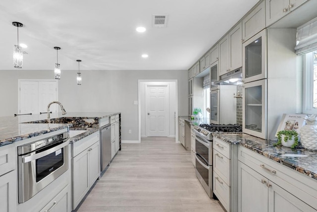 kitchen featuring light wood finished floors, visible vents, under cabinet range hood, appliances with stainless steel finishes, and a sink