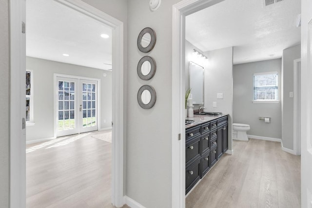 bathroom featuring wood finished floors, baseboards, double vanity, a sink, and toilet