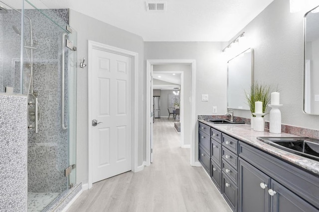 bathroom with visible vents, a stall shower, a sink, wood finished floors, and double vanity