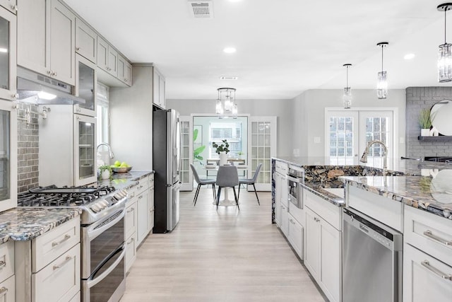 kitchen featuring visible vents, under cabinet range hood, decorative backsplash, appliances with stainless steel finishes, and an inviting chandelier