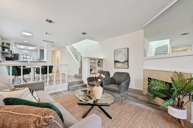 living area with stairway, a textured ceiling, visible vents, and wood finished floors