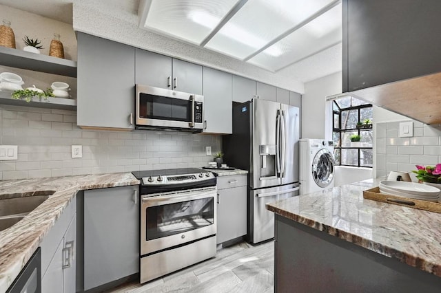 kitchen featuring tasteful backsplash, gray cabinetry, washer / clothes dryer, and stainless steel appliances