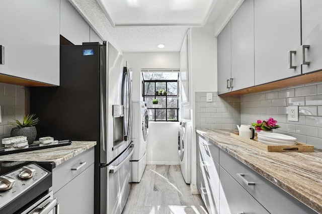 kitchen with light stone counters, stainless steel appliances, washer / clothes dryer, and decorative backsplash