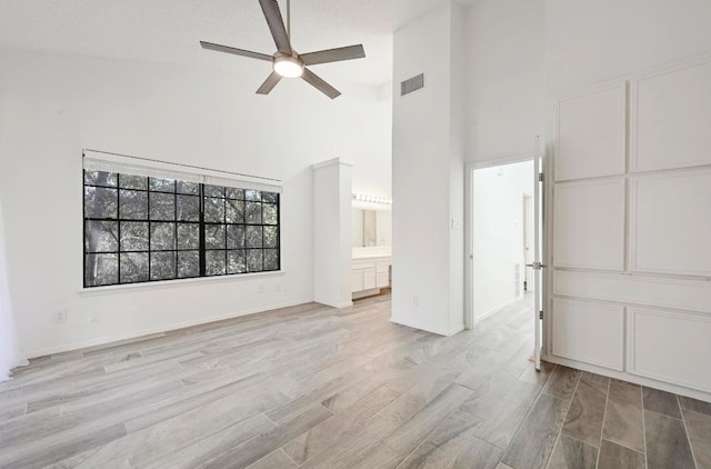 interior space featuring a ceiling fan, visible vents, light wood finished floors, baseboards, and a high ceiling