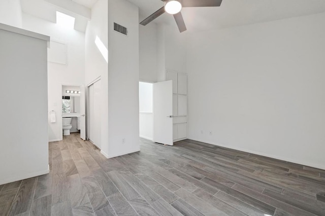 interior space with wood finished floors, baseboards, visible vents, ceiling fan, and a towering ceiling