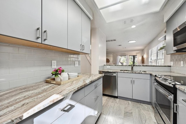 kitchen featuring a sink, visible vents, light stone counters, and appliances with stainless steel finishes