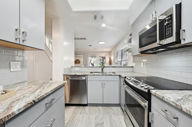 kitchen with visible vents, gray cabinetry, light stone countertops, stainless steel appliances, and a sink