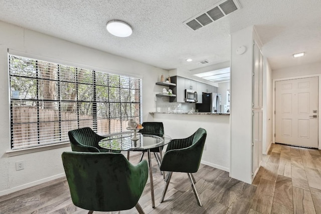 dining space featuring visible vents, baseboards, a textured ceiling, and wood finished floors