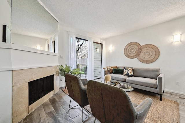 living room with a fireplace, a textured ceiling, baseboards, and wood finished floors