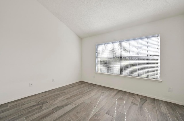 spare room with vaulted ceiling, a textured ceiling, baseboards, and wood finished floors