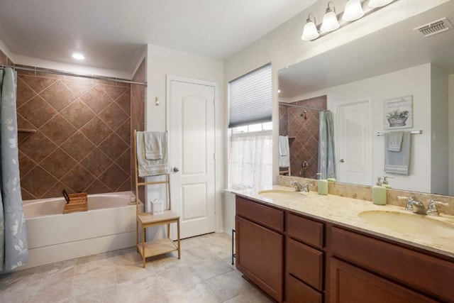 bathroom featuring double vanity, visible vents, tiled shower / bath, and a sink