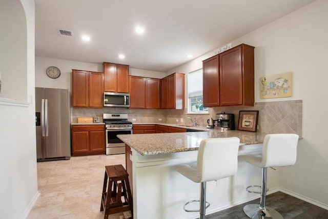 kitchen with visible vents, backsplash, light stone countertops, a peninsula, and stainless steel appliances