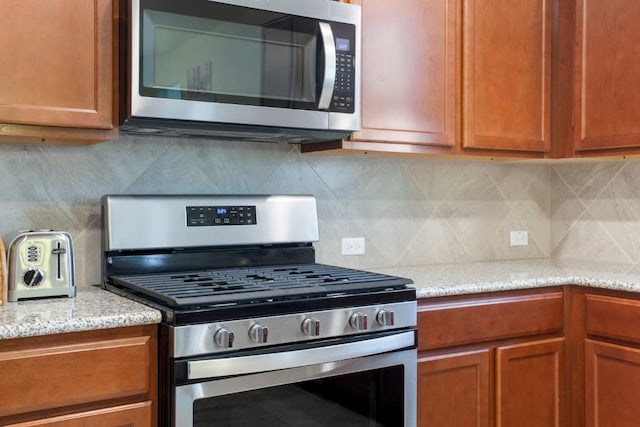 kitchen with backsplash, brown cabinets, stainless steel appliances, and light stone countertops