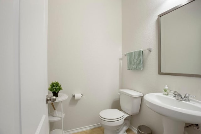 half bath with toilet, baseboards, and a sink