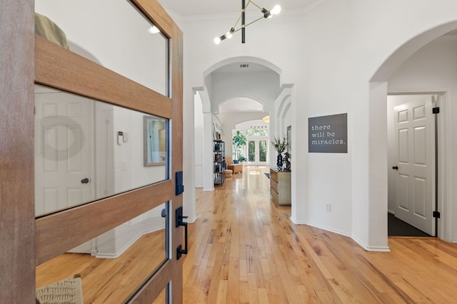 corridor featuring a notable chandelier, arched walkways, light wood-style floors, and ornamental molding