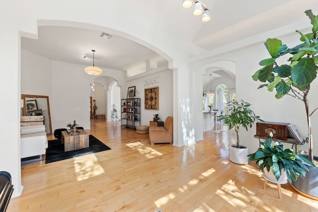 foyer entrance with visible vents, arched walkways, lofted ceiling, and wood-type flooring