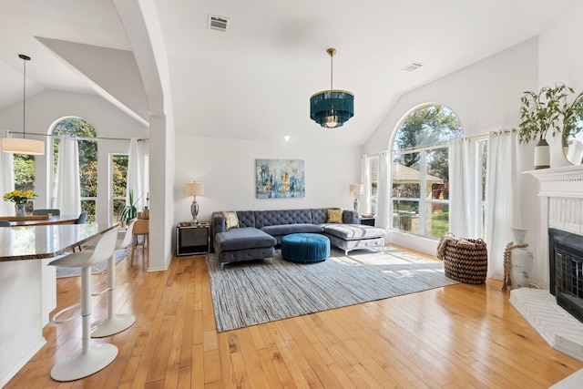 living room featuring visible vents, a brick fireplace, lofted ceiling, and light wood-style floors