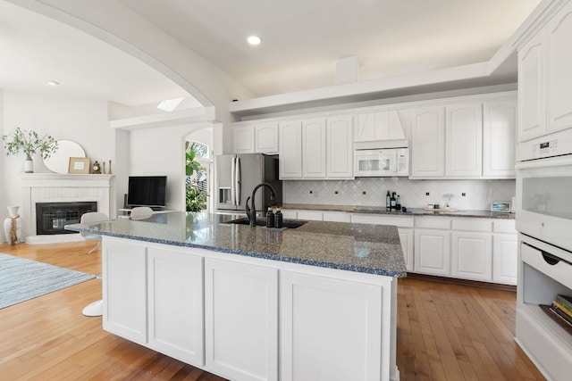 kitchen with dark stone countertops, arched walkways, white appliances, white cabinetry, and a sink