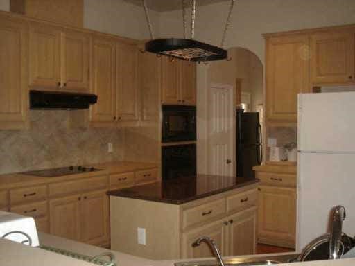 kitchen featuring backsplash, a center island, under cabinet range hood, arched walkways, and black appliances