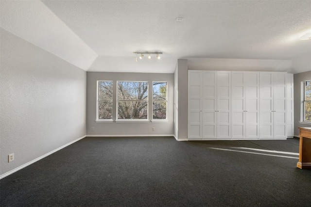 interior space featuring dark colored carpet, baseboards, plenty of natural light, and a textured ceiling