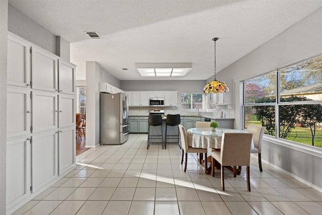 dining room featuring light tile patterned flooring, visible vents, a textured ceiling, and baseboards