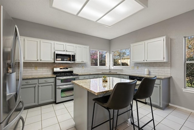 kitchen with tasteful backsplash, gray cabinetry, stainless steel appliances, and light stone countertops