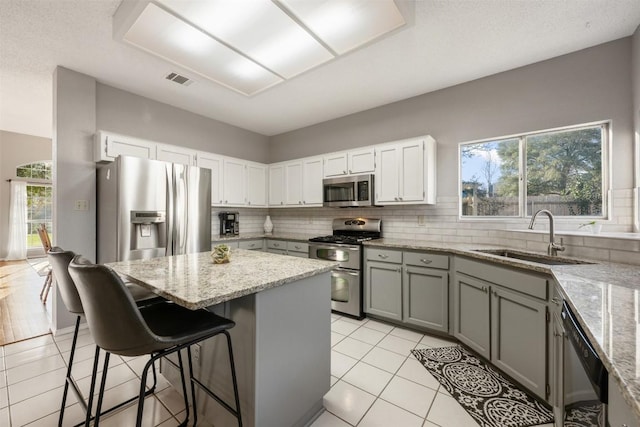 kitchen featuring a sink, a kitchen island, stainless steel appliances, decorative backsplash, and light stone countertops