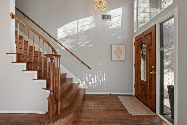 foyer entrance featuring a healthy amount of sunlight, wood finished floors, visible vents, baseboards, and stairs