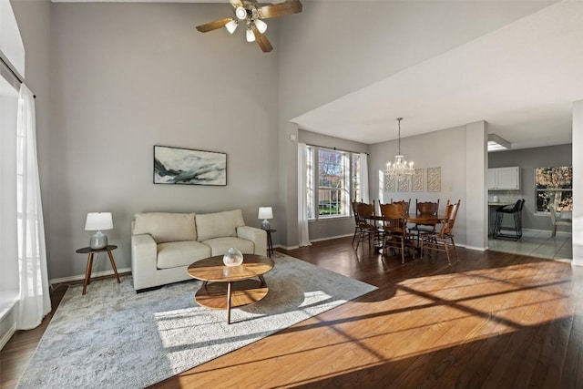 living room with a towering ceiling, ceiling fan with notable chandelier, baseboards, and wood finished floors