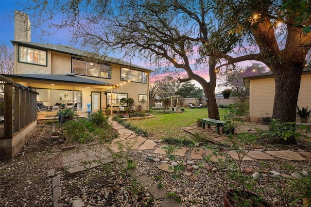 back of property at dusk with a yard, a patio, a chimney, and fence