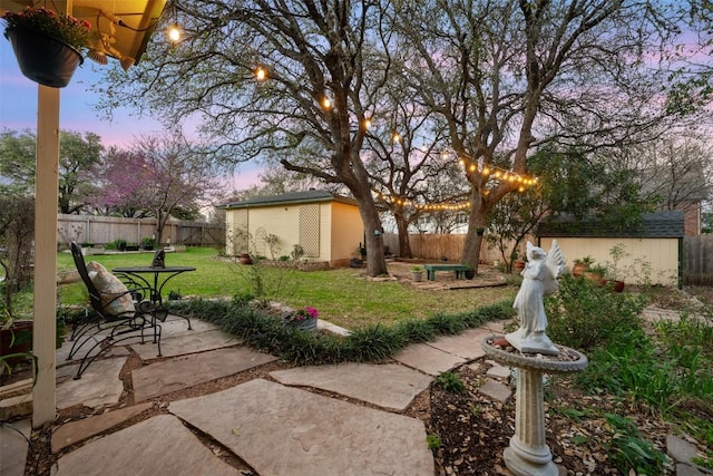 yard at dusk featuring a fenced backyard, a patio, a storage unit, and an outdoor structure