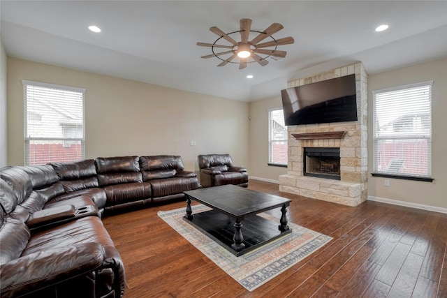 living area with a ceiling fan, wood finished floors, recessed lighting, a stone fireplace, and baseboards