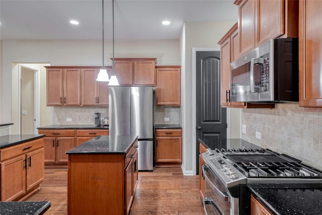 kitchen with hanging light fixtures, dark stone counters, stainless steel appliances, and light wood finished floors