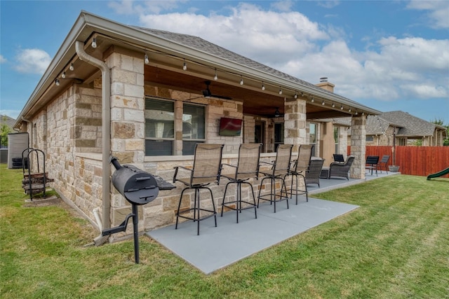 rear view of house with outdoor dry bar, fence, a yard, a patio area, and stone siding