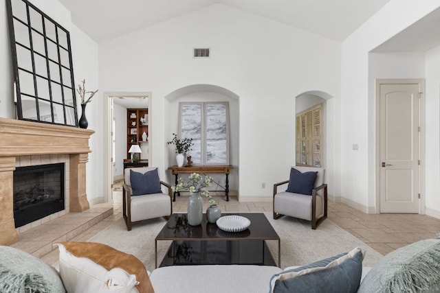 living room featuring visible vents, baseboards, high vaulted ceiling, and a tile fireplace