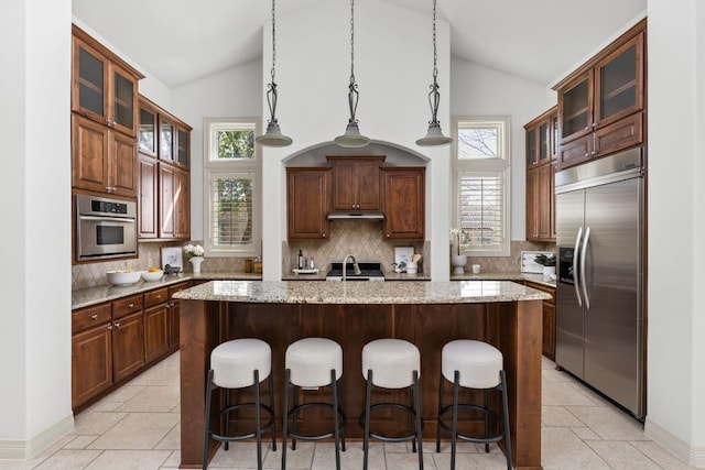 kitchen with a breakfast bar, an island with sink, under cabinet range hood, and stainless steel appliances