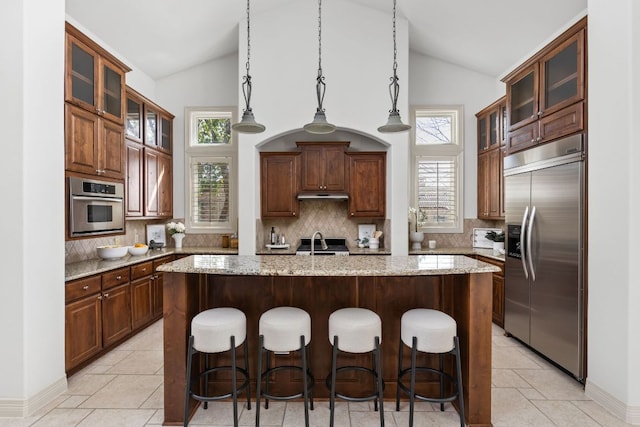 9100 Calera Dr Unit 10, Austin, TX 78735 - kitchen with appliances with stainless steel finishes, under cabinet range hood, decorative backsplash, a kitchen island with sink, and plenty of natural light