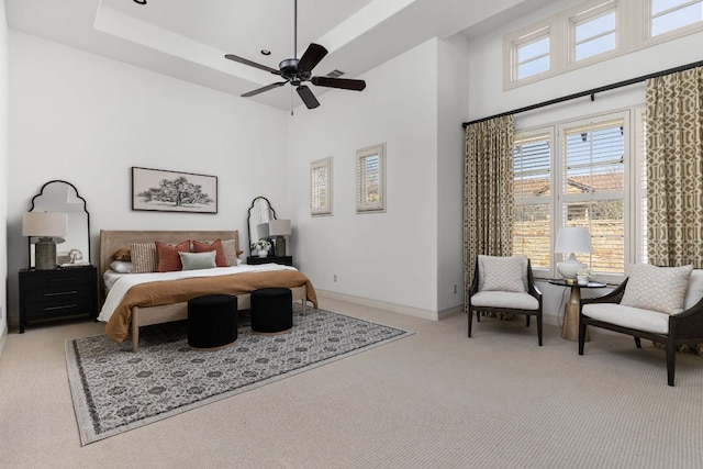 bedroom with a ceiling fan, baseboards, a tray ceiling, a towering ceiling, and light colored carpet