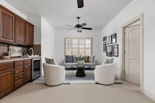 sitting room featuring baseboards, light colored carpet, beverage cooler, and a ceiling fan