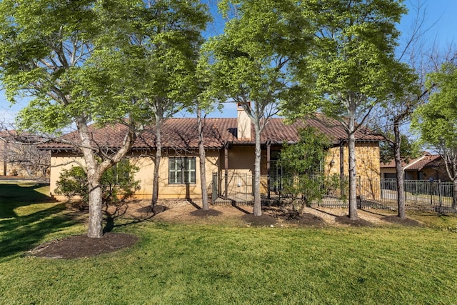 back of property with fence, a chimney, stucco siding, a tiled roof, and a lawn