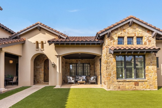 back of house with a tiled roof, stone siding, a lawn, and a patio area