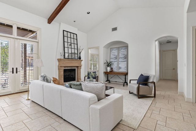 living room featuring stone tile floors, visible vents, high vaulted ceiling, a fireplace, and arched walkways