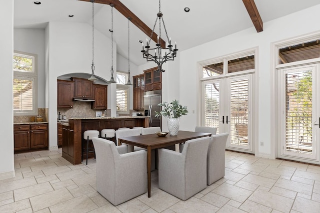 dining space featuring beam ceiling, stone tile floors, plenty of natural light, and high vaulted ceiling